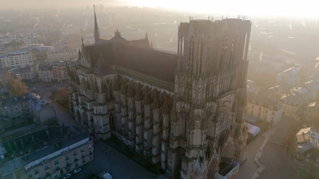 Aerial view of Reims Cathedral in France, glowing in soft golden morning light. This Gothic masterpiece is surrounded by the charming historic cityscape of Reims.