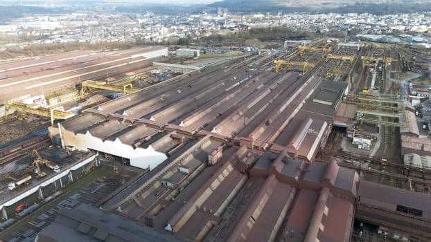 High-angle aerial view of a large steel manufacturing facility in Esch-sur-Alzette, Luxembourg, featuring warehouses, production halls, cranes, railway tracks, and industrial infrastructure.