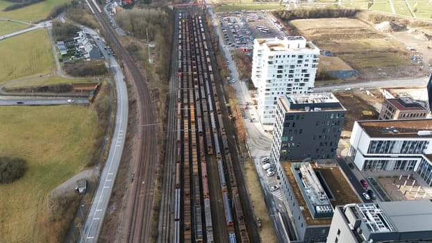 High-angle aerial view of Esch-sur-Alzette, Luxembourg, featuring a railway yard with parked freight trains, modern residential and commercial buildings, roads, and surrounding green spaces.