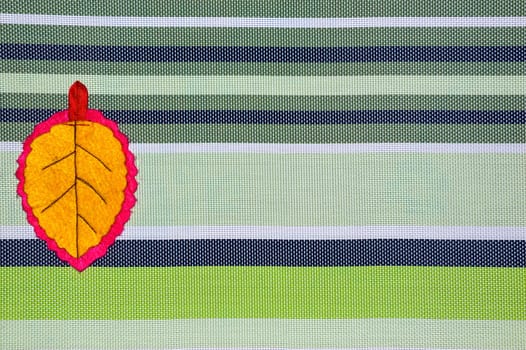 Yellow leaf handmade of fabric on striped background with copy space