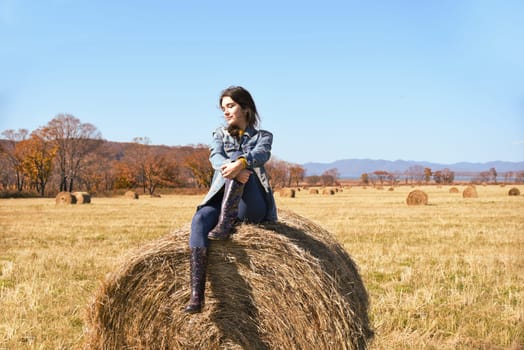 Young brunette woman sitting on top of haystack in field