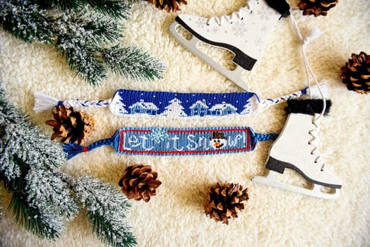 Woven friendship bracelets with alpha patterns Snowy night with houses and Let it snow. Handmade of thread, on  background with spruce cones,