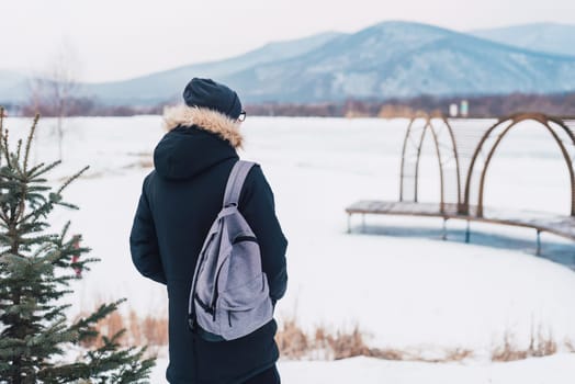 Young man solo traveler standing alone with backpack on winter background.