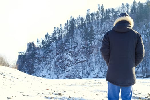 Man in warm clothes standing in the forest and looking at snowy mountains. winter, Russia.