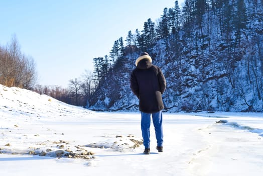 Man in warm clothes standing in the forest and looking at snowy mountains. winter, Russia.