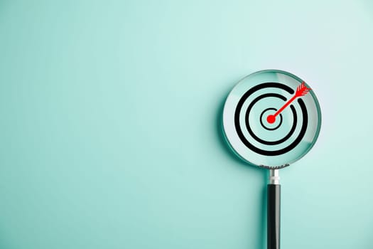 In this stock photo, a target board is magnified through a glass lens, symbolizing the business objective, target search concept, and achieving success. Isolated on a background with copy space.