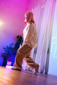 A young dancer showcases her talent in a brightly lit studio featuring colorful lighting. She wears comfortable clothing, executing fluid movements with confidence and grace.