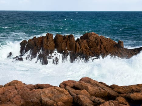 Waves crashing against rocky coastline with blue ocean sky.