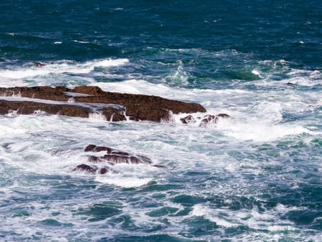 Waves crashing on rocky seashore under clear blue sky.