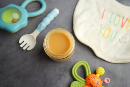 A jar of homemade baby food rests near colorful feeding accessories.
