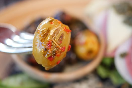 A fork holds a flavorful olive topped with herbs and spices, inviting taste.