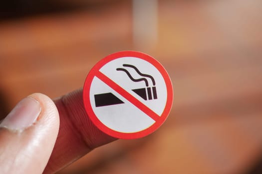 A hand displays a no smoking sign against a wooden backdrop.