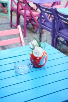 Colorful outdoor seating features a vase with flowers on a blue table.