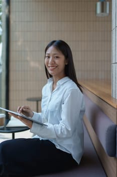 Young woman sitting in a modern caf, smiling and using a tablet with a stylish interior design in the background.