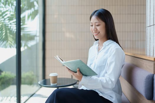 Young woman enjoying a relaxing moment while reading a book in a modern cafe with natural light and a coffee.