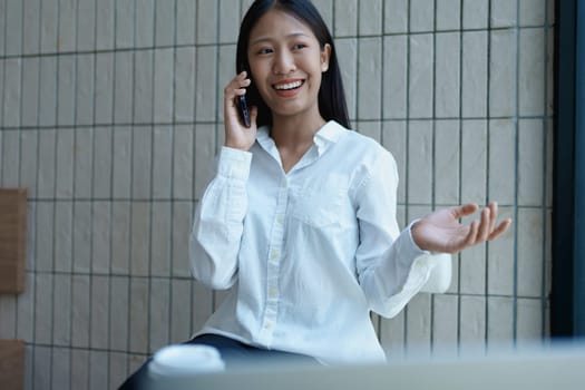 Young woman smiling while talking on smartphone in a modern workspace, expressing joy and communication with hand gestures.