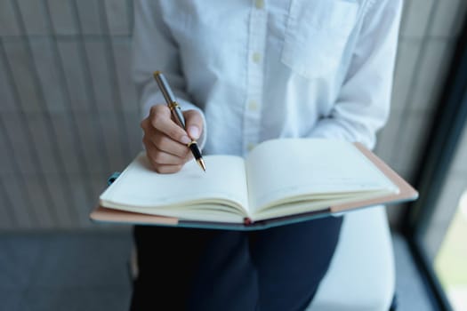 Individual writing in notebook with pen in modern office environment, focused on creative and productive work.