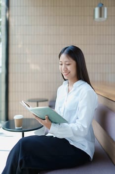 Young woman enjoying a peaceful moment reading a book in a modern coffee shop setting with natural light.