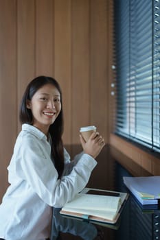 Young woman enjoying coffee in cozy modern workspace with natural light and stylish wood interior design.