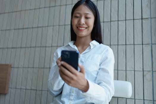 Young woman smiling while using smartphone in modern indoor setting with natural light and neutral background.