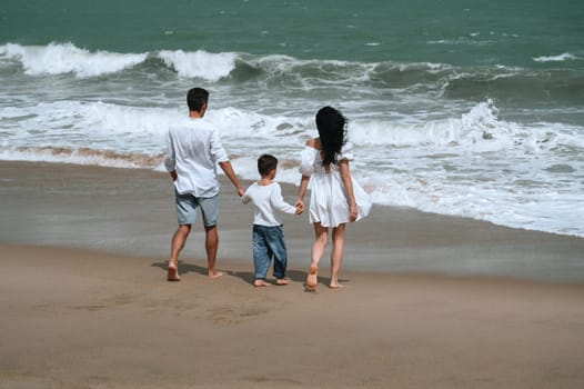 back of family with a child boy son walking along the beach by the sea in summer