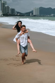 A beautiful young couple in love runs along the beach by the sea in summer. Piggyback ride