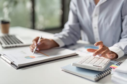 A finance professional uses a calculator to analyze data while reviewing reports, demonstrating focus and efficiency in a professional setting.