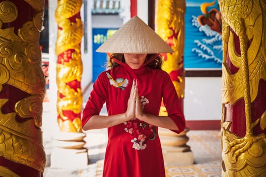Asian young woman in a traditional Vietnamese hat and costume prays at a temple on a Buddhist pagoda in Vietnam in Asia