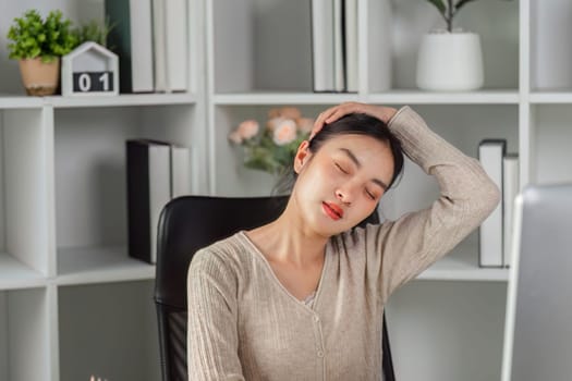 A young woman stretches her neck at her desk, relieving tension and promoting wellness in her modern office environment.