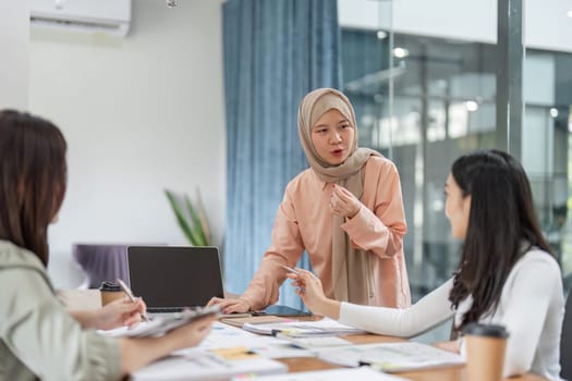 A diverse group of women brainstorms and discusses project ideas during a meeting in a contemporary office setting.