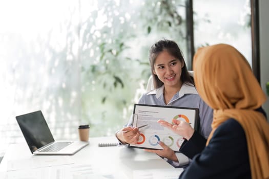 A woman presents financial data on a tablet while another listens, fostering collaboration in a professional setting.