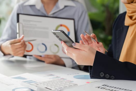 Diverse professionals analyze financial reports while using a smartphone for strategy planning, showcasing teamwork and technology.