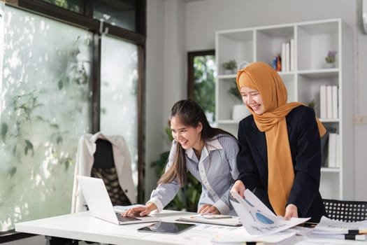 Two diverse women in finance joyfully review financial reports together, highlighting collaboration and success in their work.