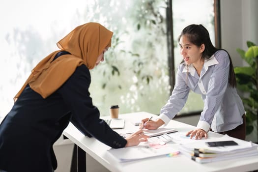 Two women collaborate on financial analysis, discussing reports and strategies in a bright office environment.