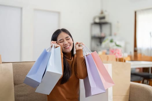A delighted young woman poses with her shopping bags, showcasing her online shopping haul in a bright home environment.