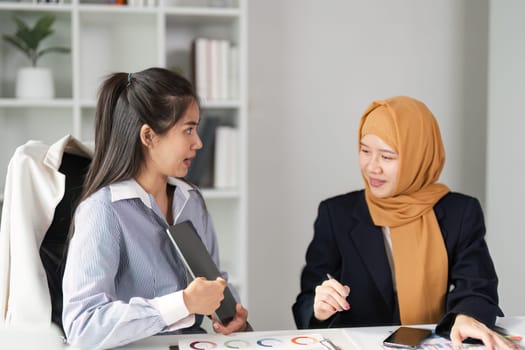 Two diverse women in finance engage in a lively discussion about financial strategies in a contemporary office environment.
