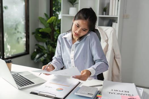 An accountant engages in a phone call while organizing financial reports and calculations, showcasing multitasking in a professional setting.