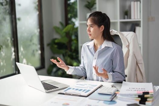 A finance professional gestures while discussing strategies during a video call, emphasizing communication and collaboration in a bright office.