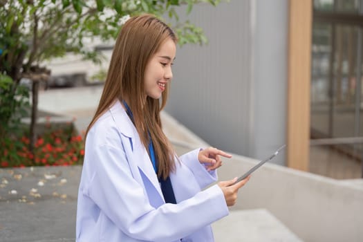 A female doctor in a lab coat uses a tablet outside, illustrating the integration of technology in modern healthcare.