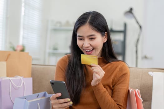 An enthusiastic woman engages in online shopping using her smartphone and credit card, surrounded by colorful shopping bags.