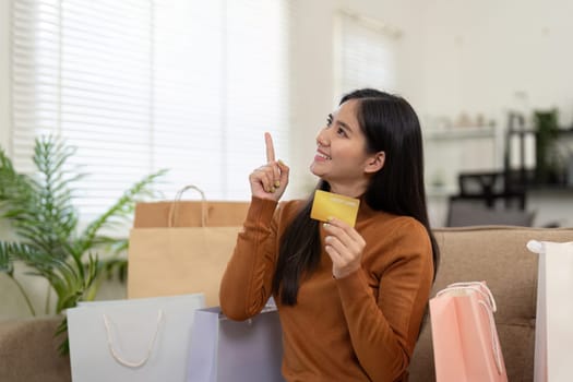 A cheerful young woman holds a credit card and points with enthusiasm, surrounded by shopping bags, highlighting the joy of online shopping.