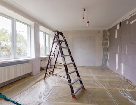 Interior renovation of a bright room with ladder and protective sheeting.