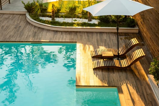 Elegant poolside wooden deck with curved lounge chairs, umbrella, and turquoise pool in a tranquil backyard