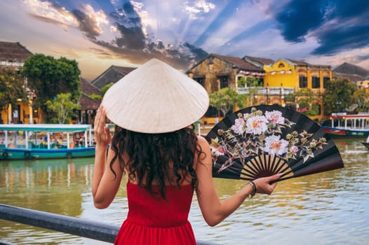back of woman tourist traveler in a Vietnamese hat with a fan on a bridge in Hoi An in Vietnam in Asia