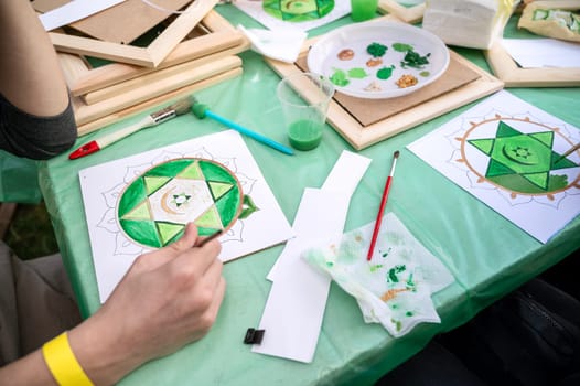woman's hand draws a mandala with green paints and a brush. drawing as a hobby. concept of communication and psychological relief, mental balance
