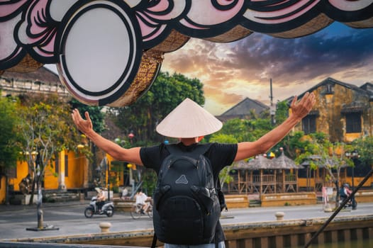 back of male tourist in a Vietnamese hat on a old bridge in ancient town in Hoi An in Vietnam in Asia