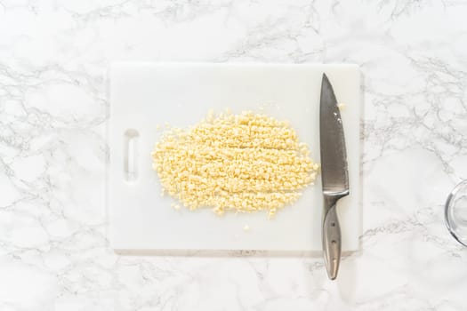 Flat lay. On a white cutting board, skillfully chopping white chocolate chips with a knife adds the perfect touch to a baking adventure.