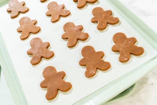 Angled view of unbaked gingerbread man cookies evenly arranged on a parchment-lined baking sheet.