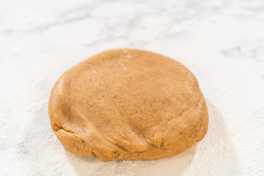 Straight-on view of amber gingerbread cookie dough resting on a floured marble countertop, prepared for the next baking step.