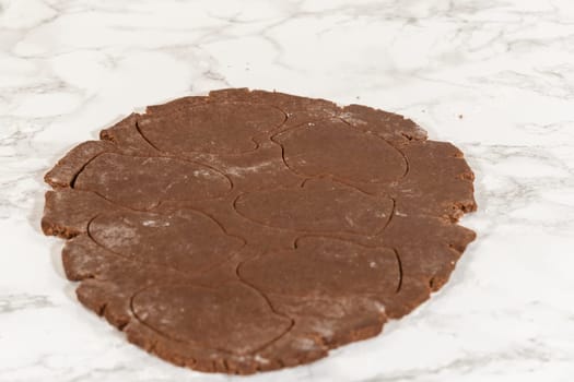 Front-facing view of hands pressing a mitten-shaped cutter into the rolled-out chocolate gingerbread dough to create cookie shapes.